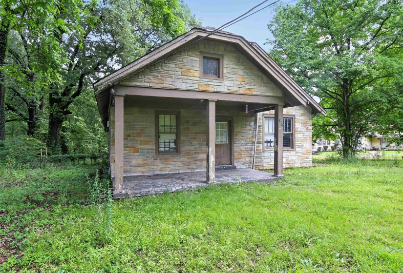 Stone exterior home featuring a covered front porch with support columns, a gabled roof, and multiple windows