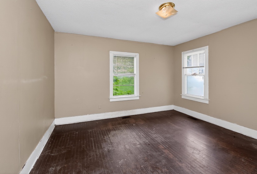 Room featuring wood-finish flooring, two windows with white trim, tan painted walls, white baseboards, and a flush-mount ceiling light fixture
