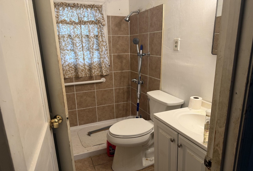 Bathroom featuring a tiled shower surround with a grab bar, a window, a white vanity with cabinet storage, and a white toilet