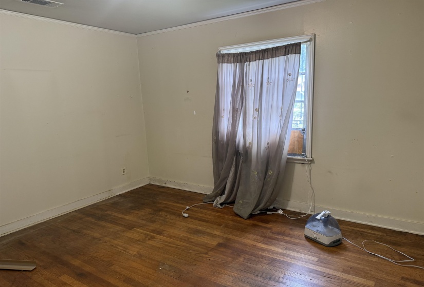 Hardwood flooring throughout featuring white baseboards and crown molding