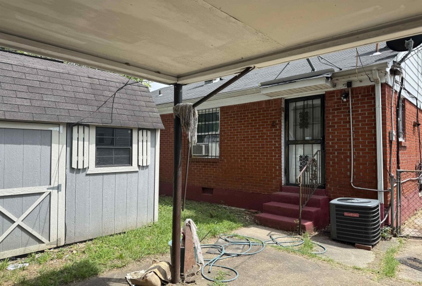 Red brick exterior with a rear entry door featuring security grating, a concrete patio area, and an external HVAC unit