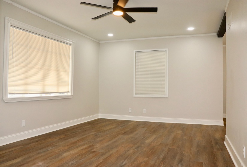Spacious room featuring wood-finish flooring, light neutral wall paint, multiple windows with blinds, recessed lighting, and a ceiling fan