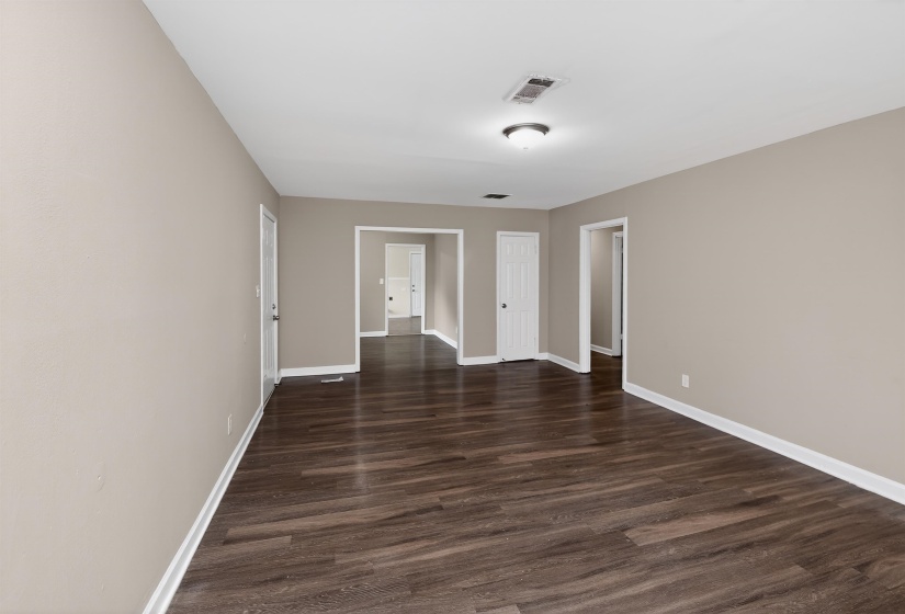 Expansive room featuring wood-finish flooring, light tan wall finishes, white baseboards, and a semi-flush mount ceiling light fixture