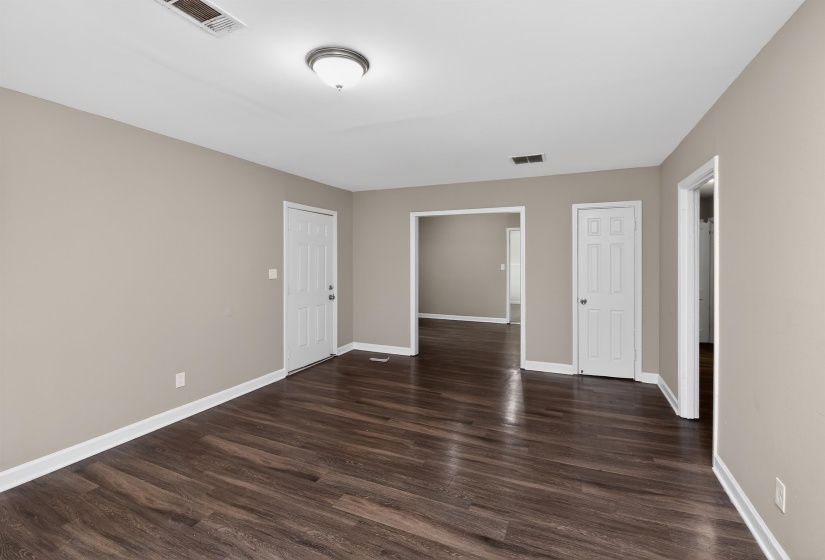 Spacious room featuring wood-finish flooring, neutral-toned walls, white trim, and multiple doorways
