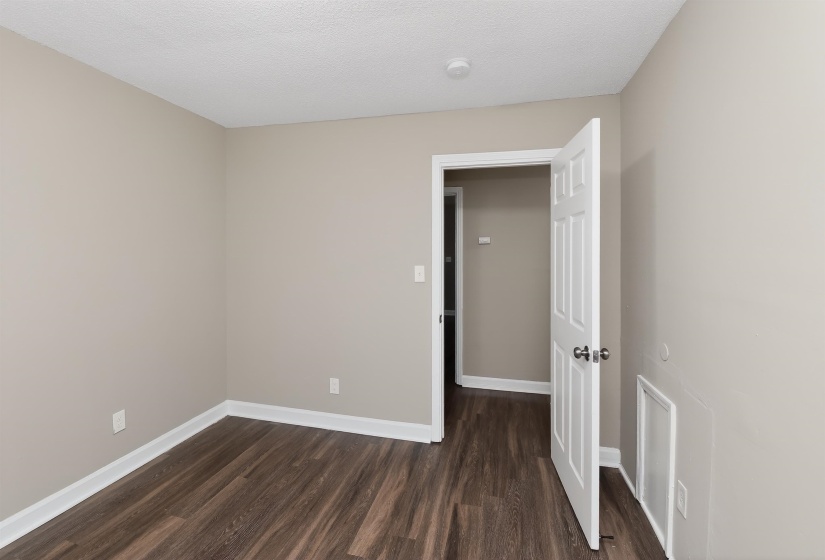 Neutral-toned interior room featuring wood-finish flooring, white baseboards, and a paneled interior door with chrome hardware