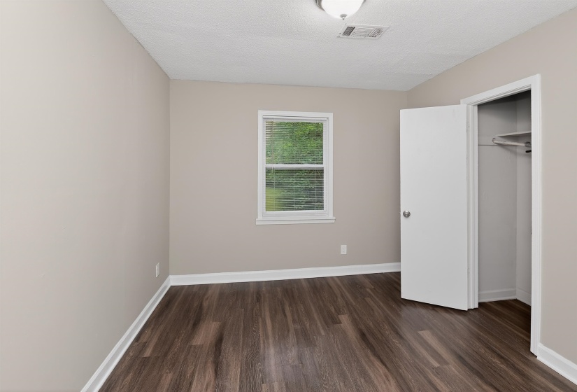 Room featuring wood-finish flooring, neutral wall paint, white trim, a single window, and a closet with an open door