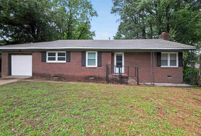 Brick exterior home featuring an attached garage with a white door, a covered front porch with metal railings, a shingled roof, and multiple windows with dark shutters