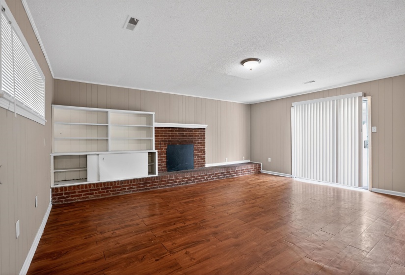 Spacious room featuring wood-finish flooring, a brick fireplace with hearth, and integrated shelving