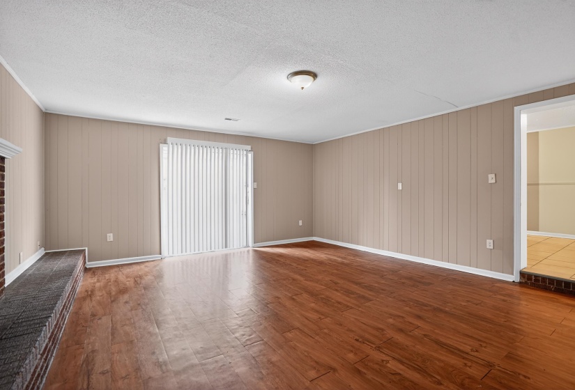 Spacious room featuring wood-finish flooring, vertical paneling, and a brick hearth