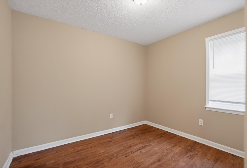 Interior space featuring wood-finish flooring, neutral wall paint, white baseboards, and a single window with blinds