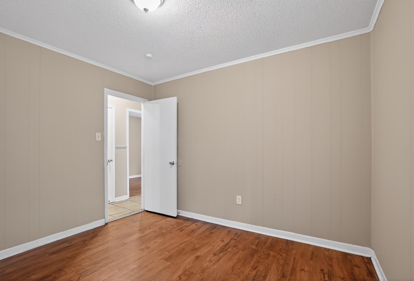Interior room featuring wood-finish flooring, light beige panel walls, white trim, and a white ceiling with a flush-mount light fixture