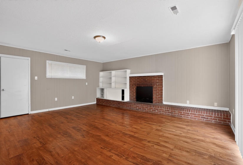 Spacious room featuring rich wood-finish flooring, a brick fireplace with a raised hearth, and built-in shelving
