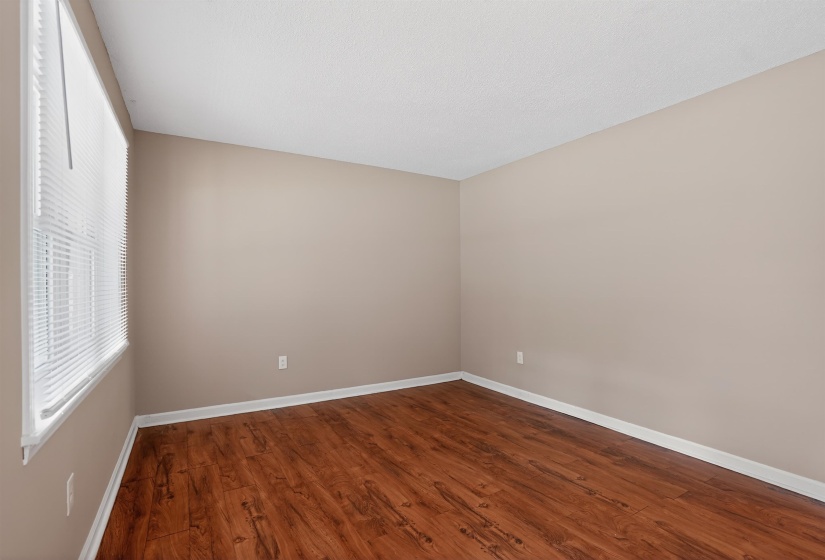 Interior room featuring wood-finish flooring, neutral wall paint, white baseboards, and a window with blinds