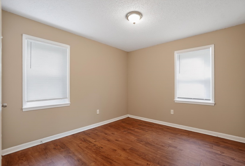Bedroom featuring wood-finish flooring, neutral wall paint, two windows with blinds, white trim, and a ceiling-mounted light fixture