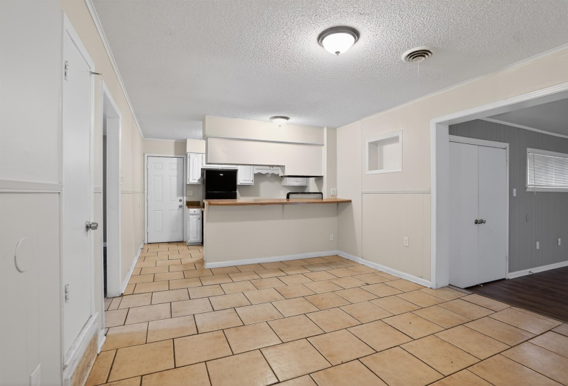 Open-concept kitchen and dining area featuring ceramic tile flooring, a breakfast bar with a wood-finish countertop, white cabinetry, and black appliances