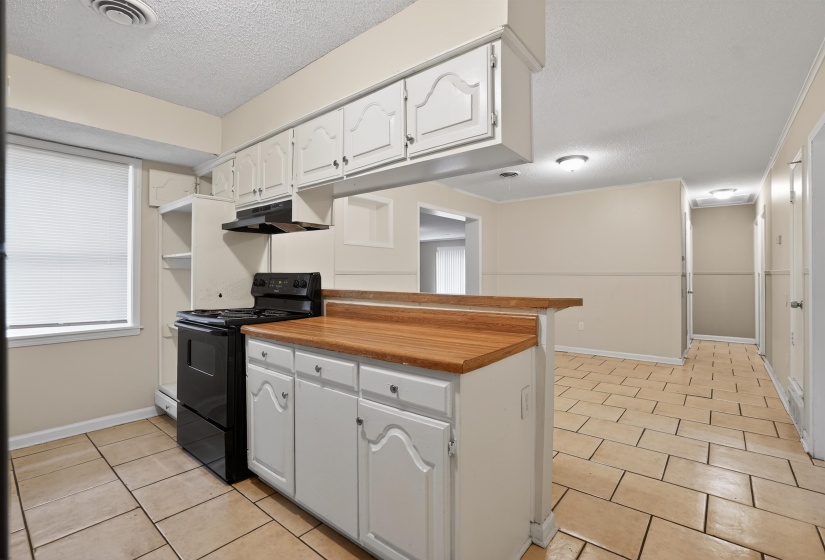 Kitchen featuring white cabinetry, a black range, and wood-finish countertops