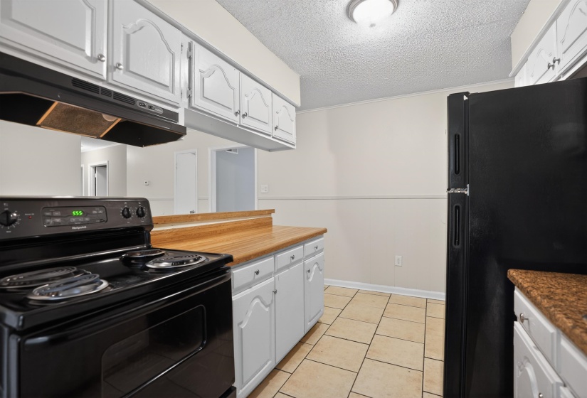 Kitchen with white cabinetry, a black electric range, and wood-finish countertops