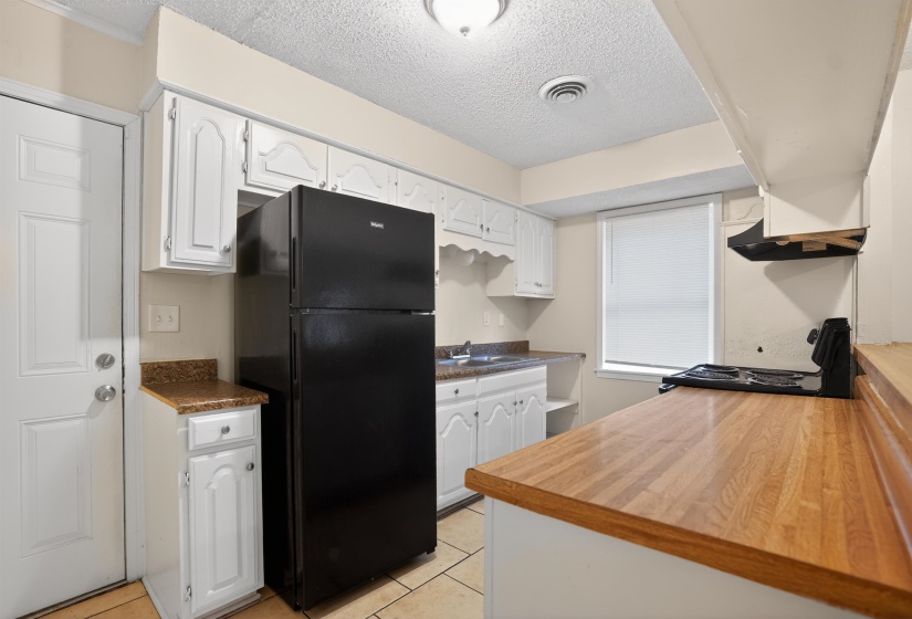Functional kitchen featuring white cabinetry, a black refrigerator, a built-in range, and wood-finish countertops
