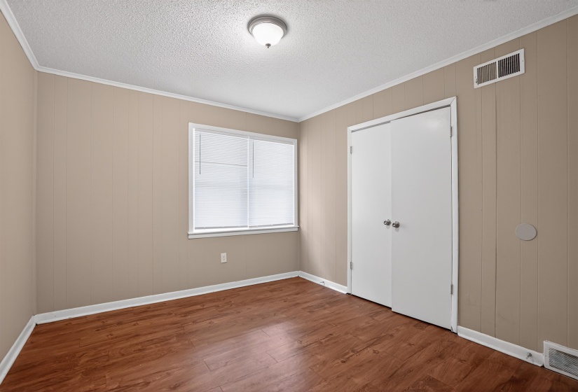 Bedroom featuring wood-finish flooring, neutral wall paneling, and a ceiling-mounted light fixture