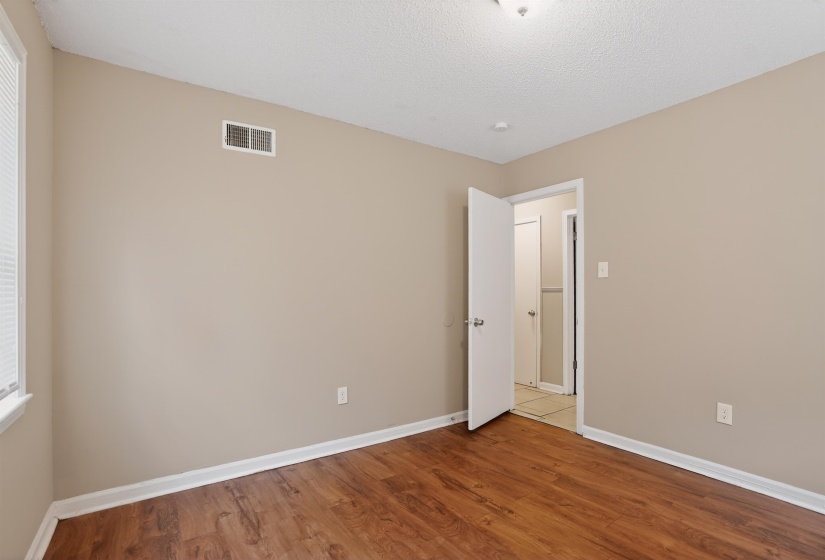 Interior room featuring wood-finish flooring, neutral wall paint, white trim, and a window with blinds