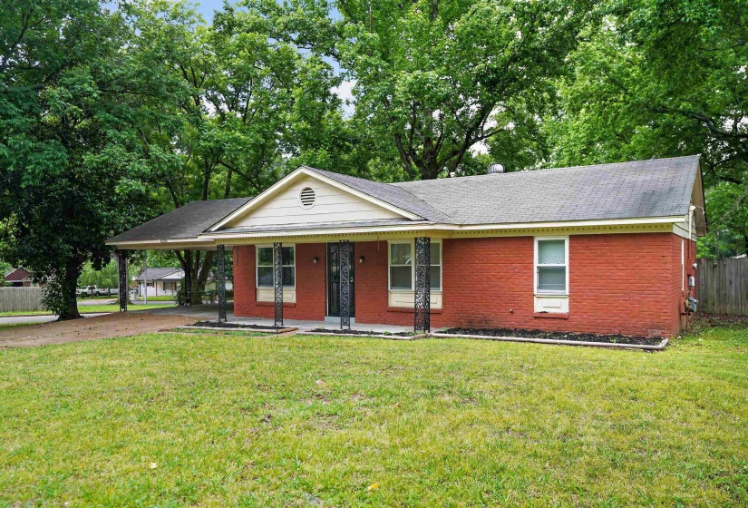 Brick exterior residence featuring a covered carport, gabled roofline, decorative wrought iron porch columns, and a landscaped foundation bed