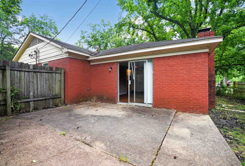 Rear exterior featuring red brick siding, a concrete patio, and a sliding glass door