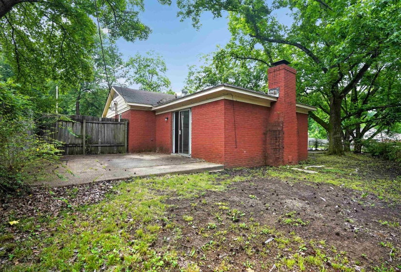 Brick exterior with a prominent brick chimney, concrete patio, sliding glass door, and partial wood fencing
