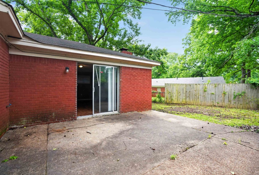 Red brick exterior featuring a patio, sliding glass door, exterior lighting, and a fenced backyard