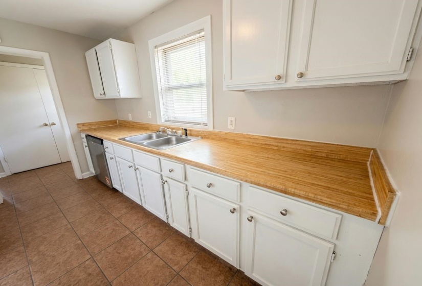 Kitchen featuring wood-finish countertops, white cabinetry, a double basin stainless steel sink, and a built-in dishwasher