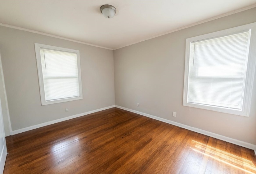 Room featuring wood-finish flooring, light grey painted walls, white trim, and two windows with blinds