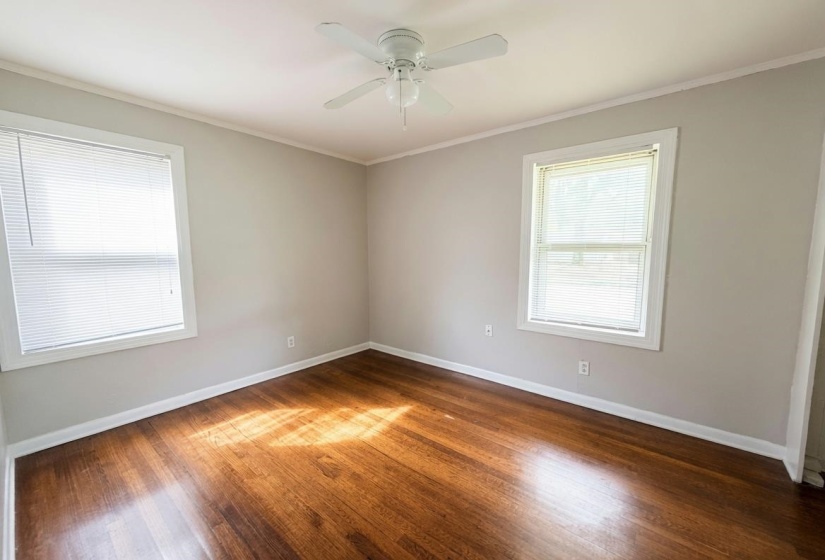 Spacious room featuring wood-finish flooring, light grey painted walls, white trim, and a white ceiling fan