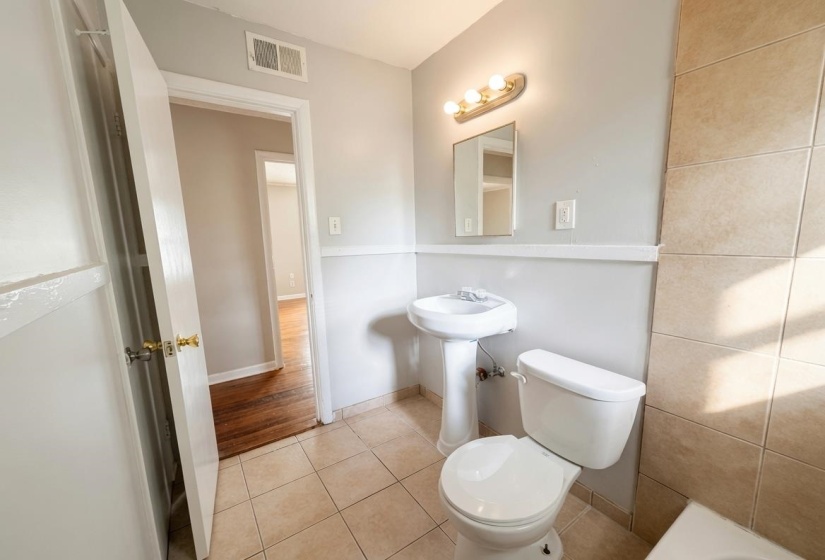 Bathroom featuring a pedestal sink, white toilet, wall-mounted mirror, and vanity light fixture