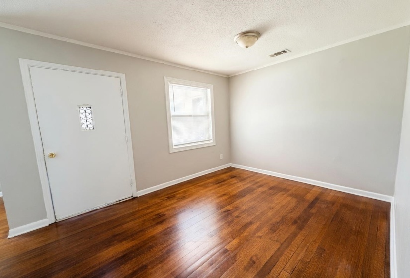 Interior room featuring rich wood-finish flooring, light gray wall paint, white baseboards, and a single window with white trim