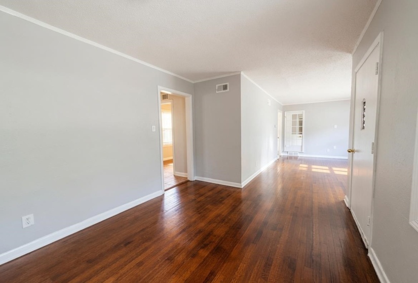 Spacious interior featuring wood-finish flooring, light gray wall paint, white baseboards, and white crown molding