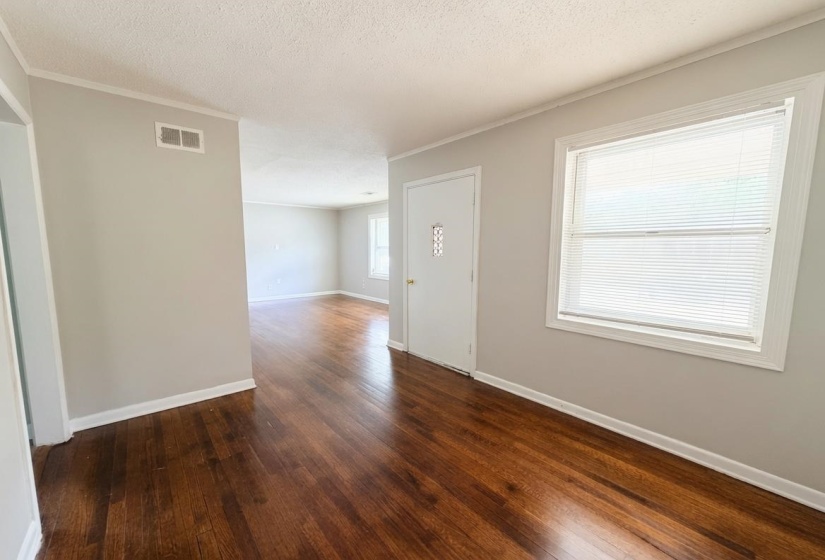 Hardwood-finish flooring extending through an open-concept interior with light neutral wall tones, white trim, and bright windows featuring blinds