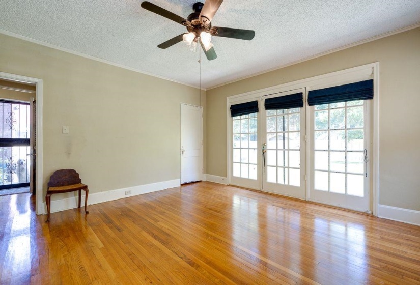 Hardwood flooring throughout featuring white baseboards, a ceiling fan with integrated lighting, and three French doors with transom windows