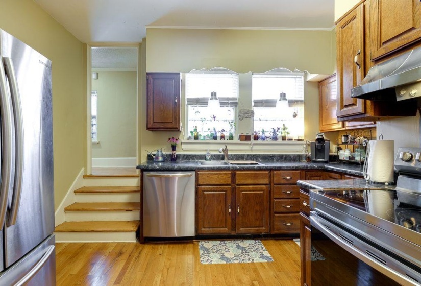 Kitchen featuring wood-finish flooring, dark perimeter countertops, and stainless steel appliances including a refrigerator, dishwasher, and range