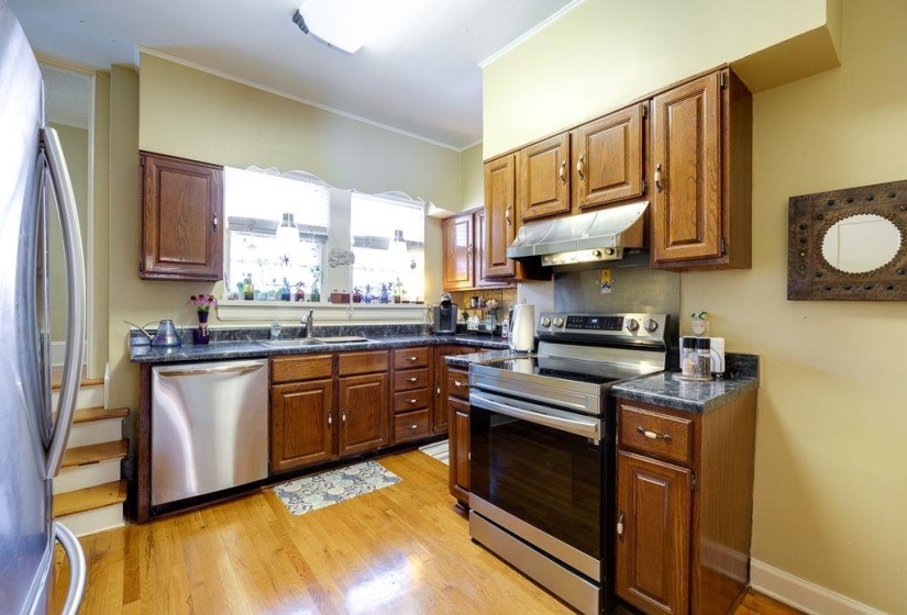 Kitchen featuring wood-finish cabinetry, stainless steel appliances, dark countertops, and light wood-finish flooring