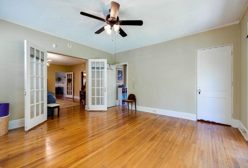 Spacious room featuring wood-finish flooring, a ceiling fan with integrated lighting, and multiple entry points including French doors