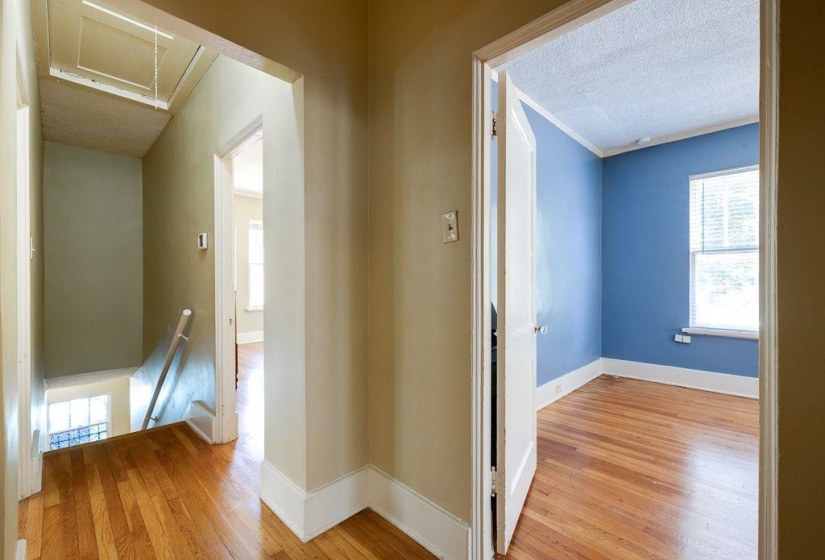 Hardwood flooring extends throughout the hallway and into a room featuring blue walls and a window with blinds