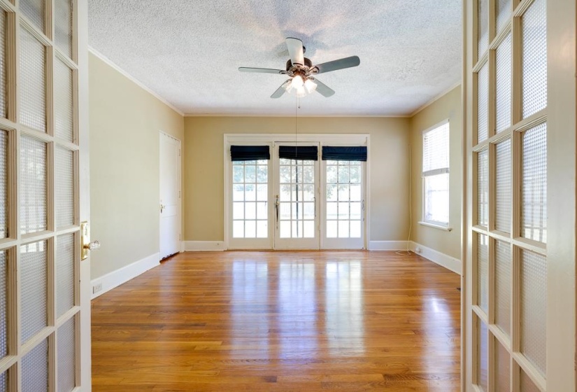 Spacious room featuring rich wood-finish flooring, a ceiling fan with integrated lighting, and multiple windows