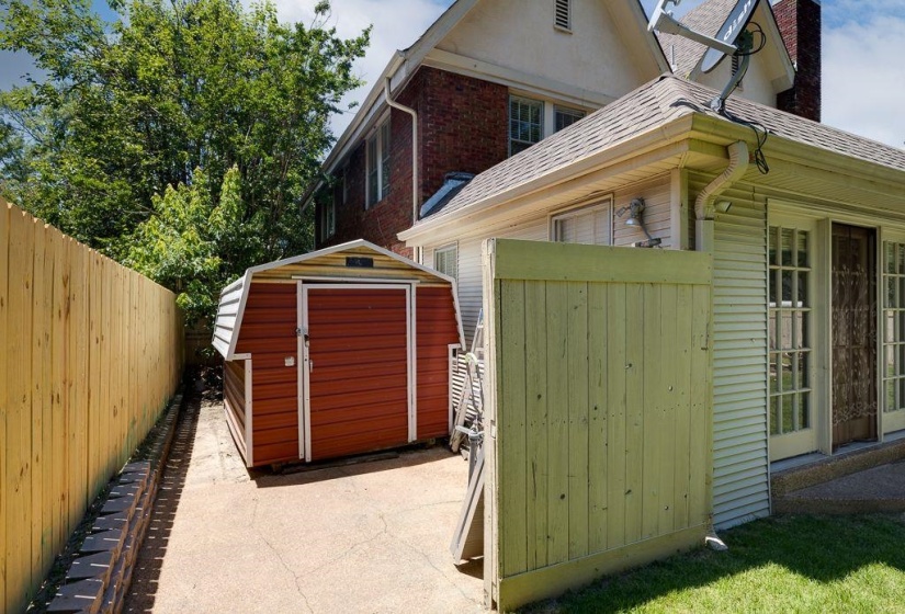 Rear exterior featuring a red storage shed, light-colored wood privacy fencing, and a concrete pathway