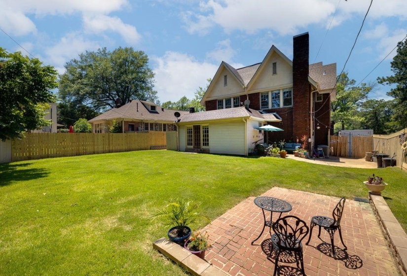 Spacious backyard featuring a large green lawn, a red brick patio, and a light-toned wood privacy fence