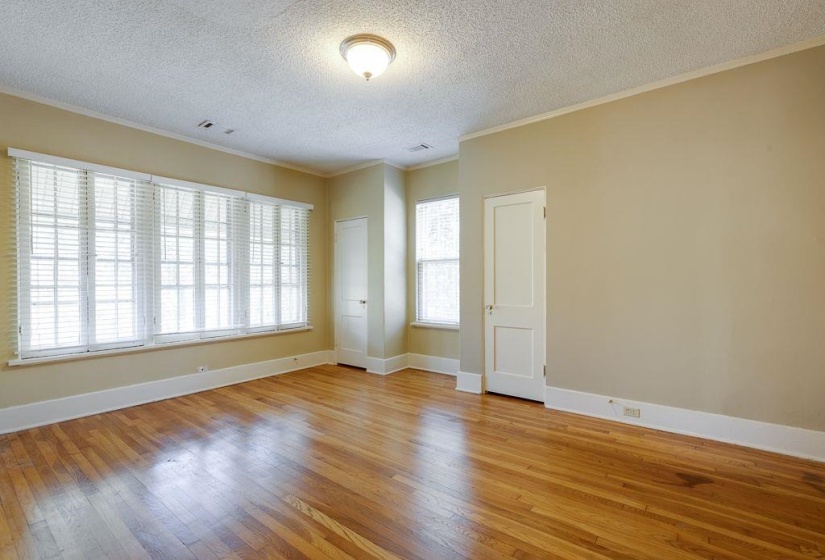 Room featuring wood-finish flooring, multiple windows with blinds, a ceiling-mounted light fixture, and two panel doors