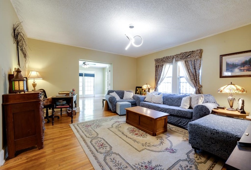 Spacious living area featuring wood-finish flooring, a decorative area rug, and an open doorway leading to a sunroom with French doors
