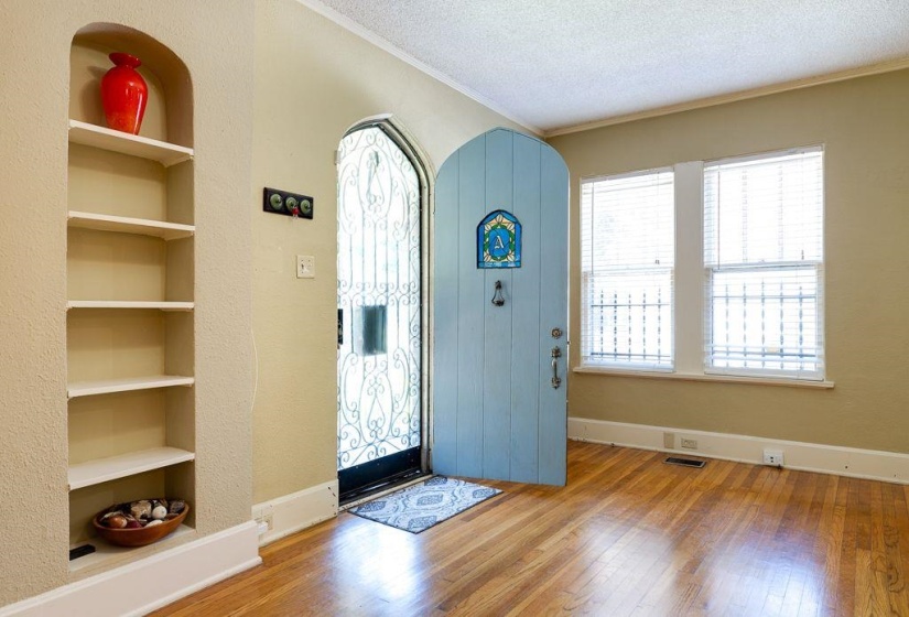 Arched entryway with a light blue door, decorative iron security door, and wood-finish flooring
