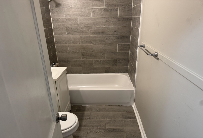 Bathroom featuring a white bathtub, gray rectangular wall tiles, and wood-finish floor tiles