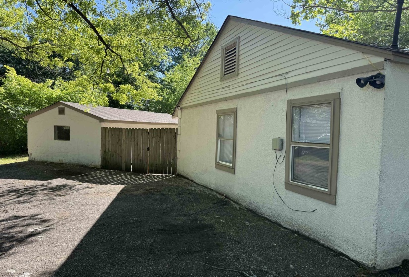 Exterior stucco siding with contrasting trim, gable roofline, and attached outbuilding with wood privacy fencing