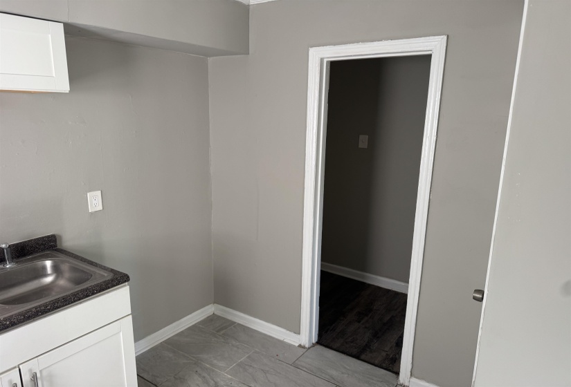 Kitchenette featuring a stainless steel sink, dark countertop, and white cabinetry