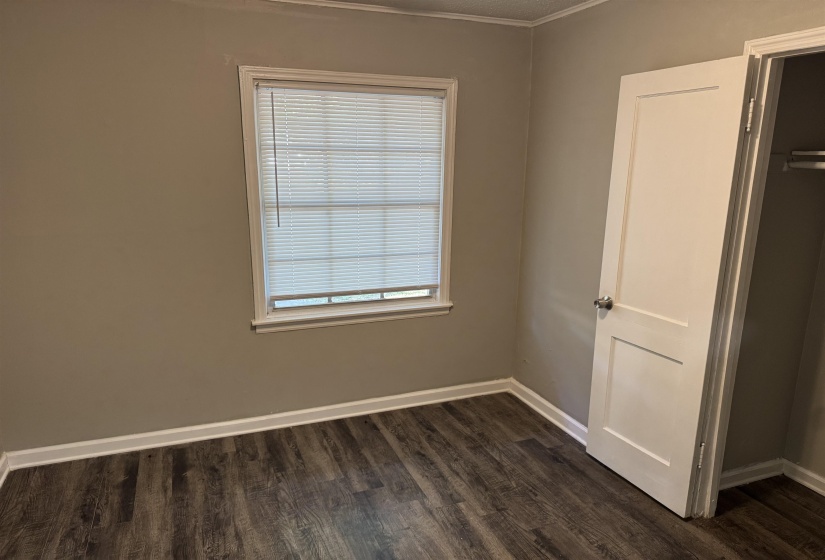 Neutral-toned room featuring wood-finish flooring, white baseboards, and a window with blinds